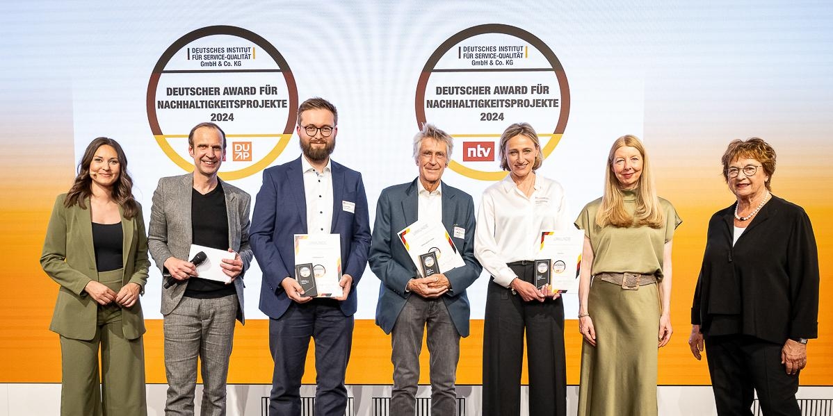 Männer und Frauen vor orangeweißem HIntergrund mit Preisen in der Hand